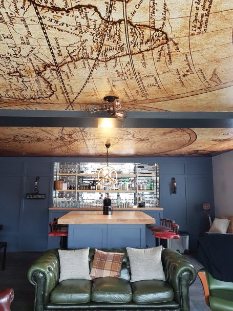 Stylish lounge with a bar, leather sofa, and a map-patterned ceiling.